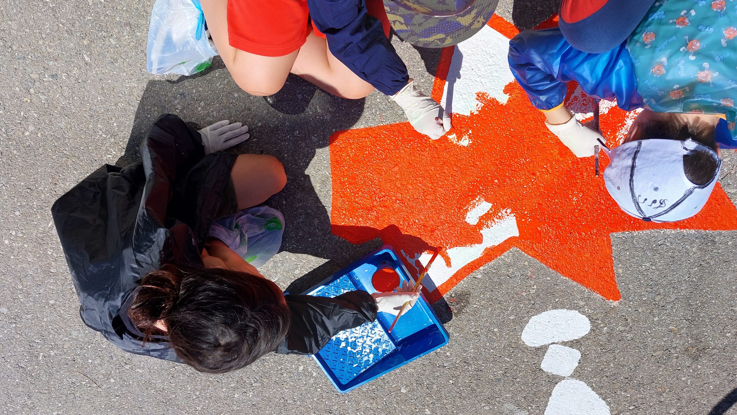 3 élèves de l'école Hauterive a Posieux sont en train de peindre une fresque dans leur cour de récréation.
