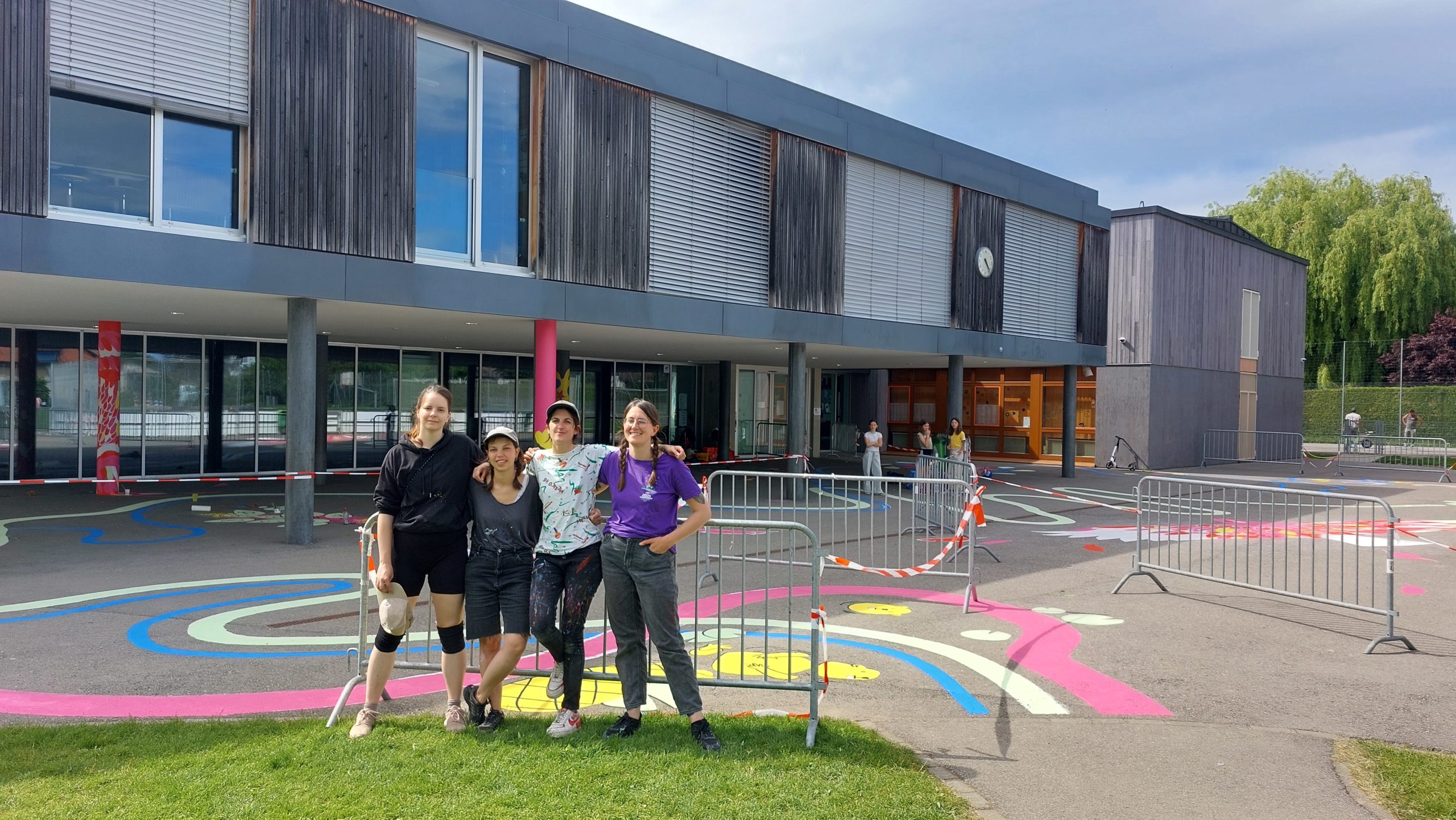 Groupe de 4 artistes de laa Maison Noctua qui ont peint la fresque scolaire qu'on voit en arrière plan.