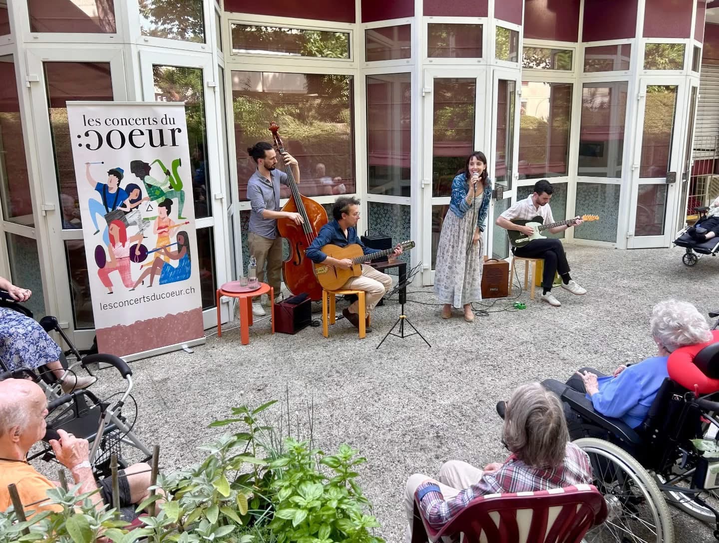 Une photo d'un concert donné dans la cour d'une résidence pour personnes âgées avec un violoncelle, 2 guitares et une chanteuse. Le rollup de l'illustration des concerts du coeur.