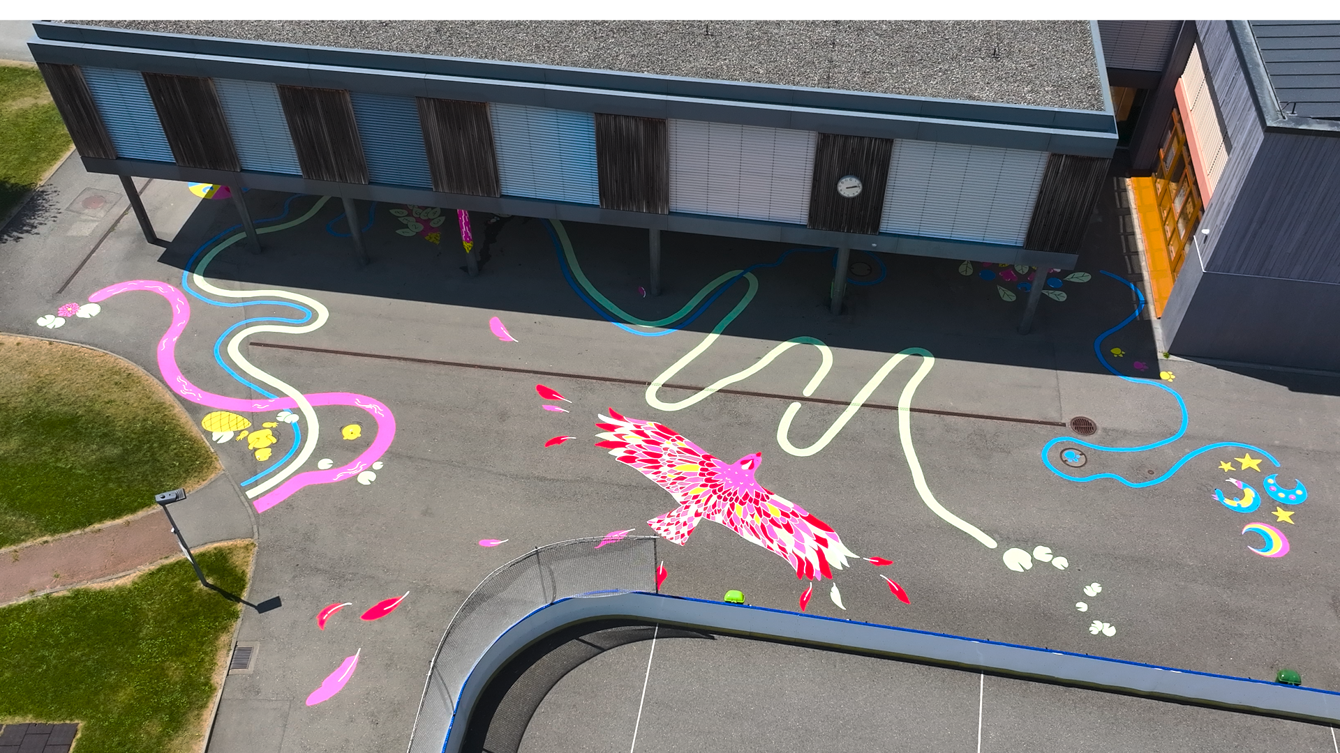 Vue depuis un drone d'une fresque peinte dans une cour de récré. On y voit des jeux ludiques, un grand aigle avec un alphabet sur ces ailes, des loups en forme de lunes.
