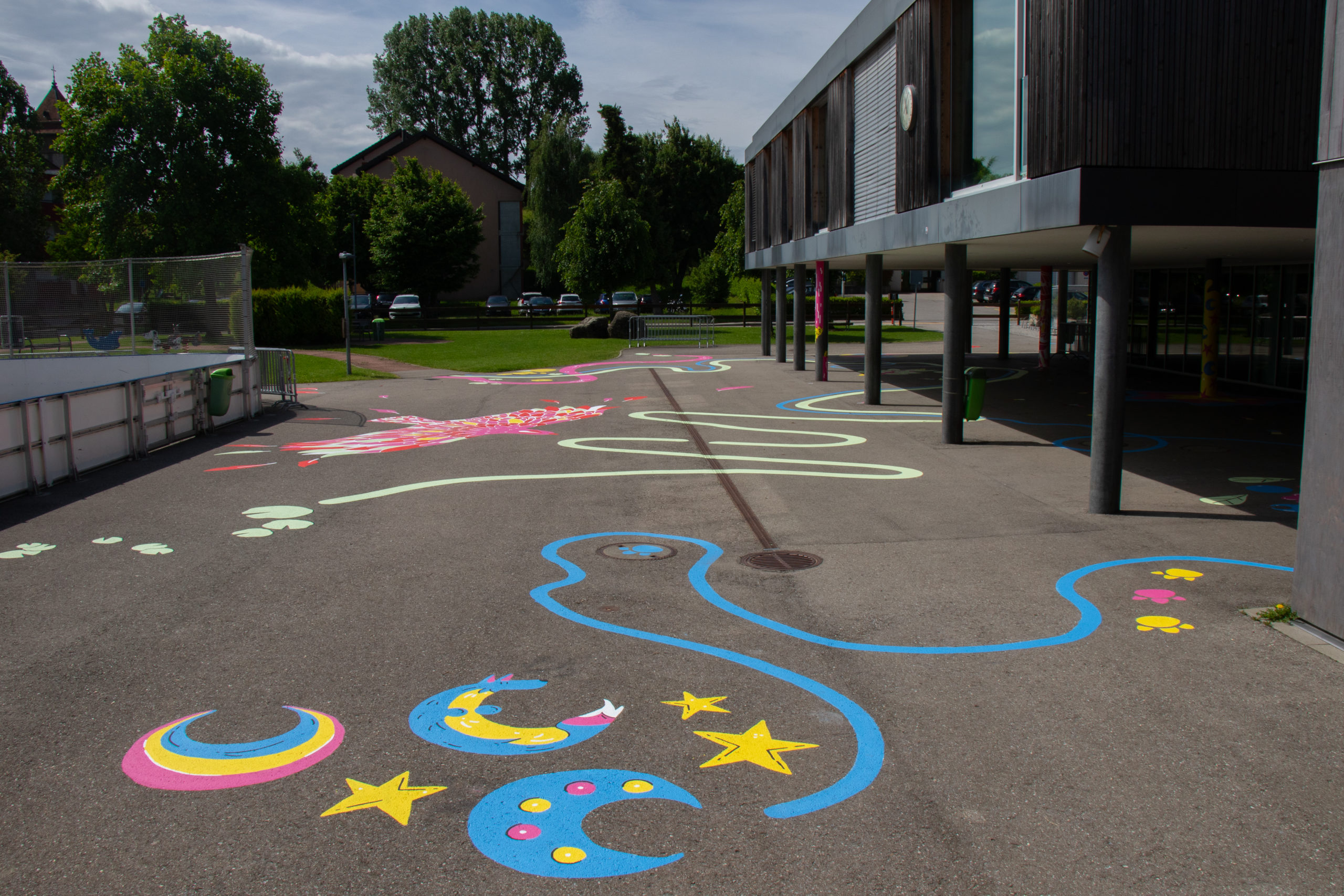 Vue d'ensemble dela cour de récréation de l'école de Posieux où on voit une fresque peinte par les éléves et 4 artistes fribourgeoise